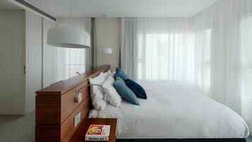 Una habitación de hotel moderna con una cama grande, un aparador de madera y una mesita de noche con un libro.