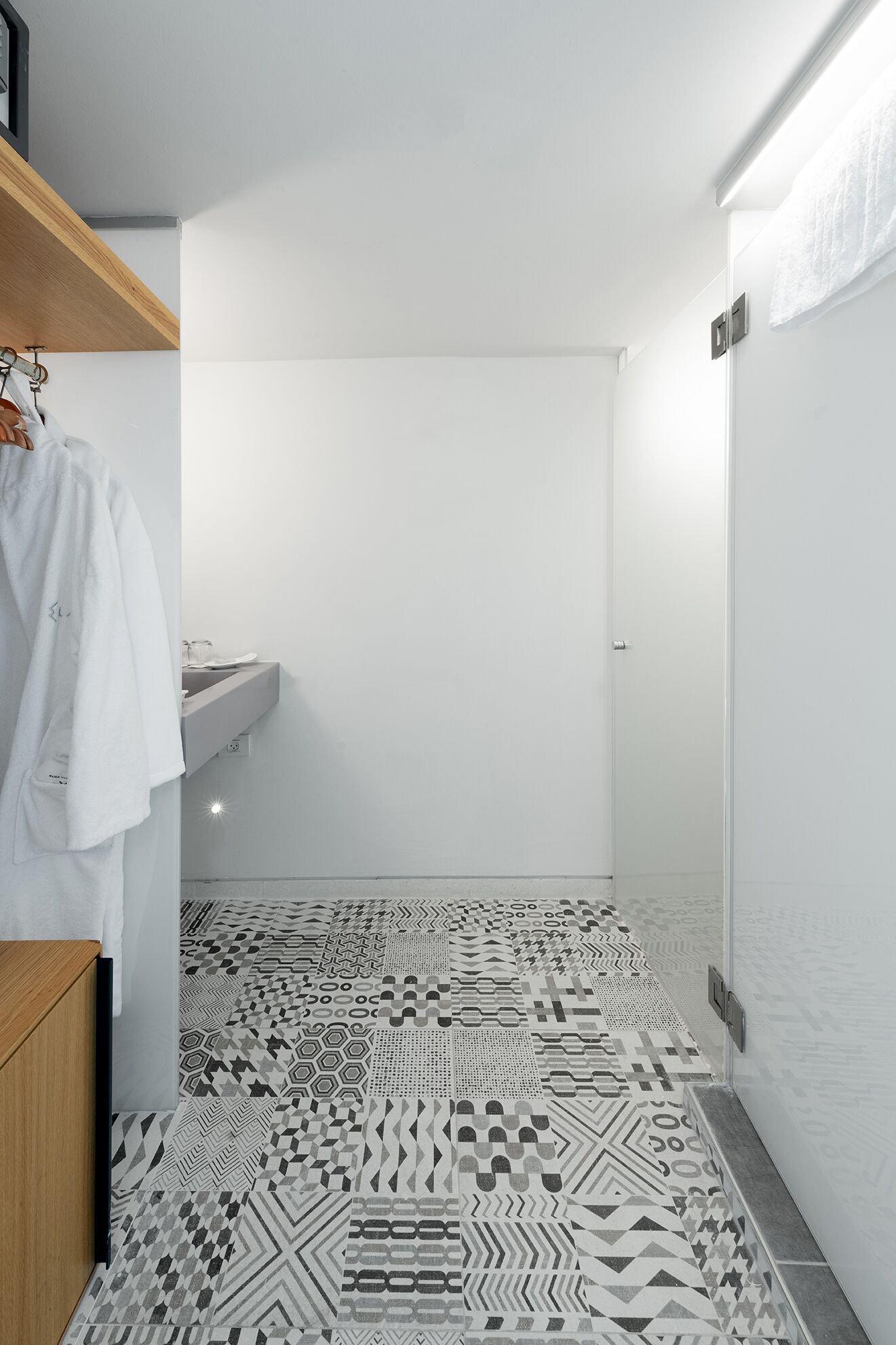 A modern bathroom with a geometric patterned floor, a wooden shelf with a white towel, and a white sink.