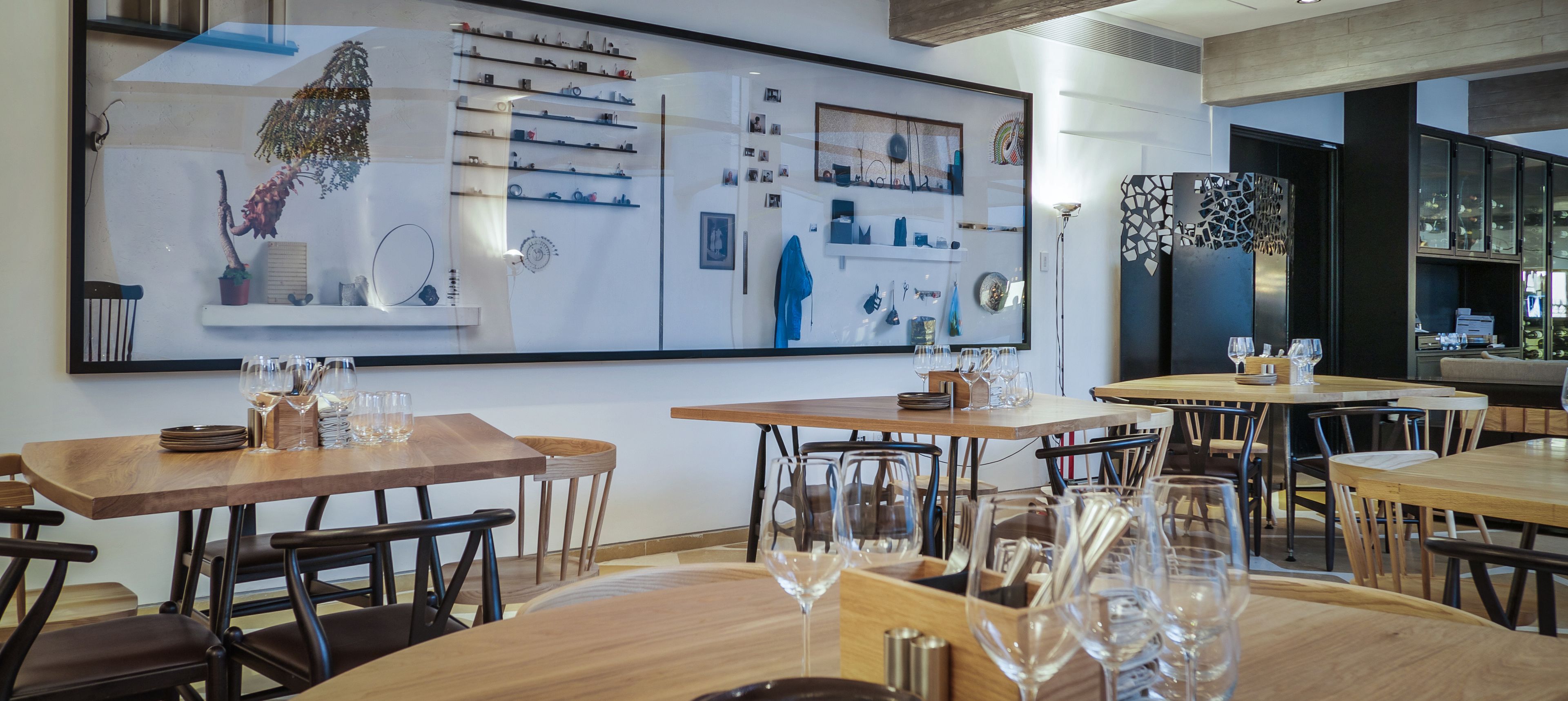 A restaurant with wooden tables and chairs, a large wall with various items displayed, and a bar area with glasses and bottles.