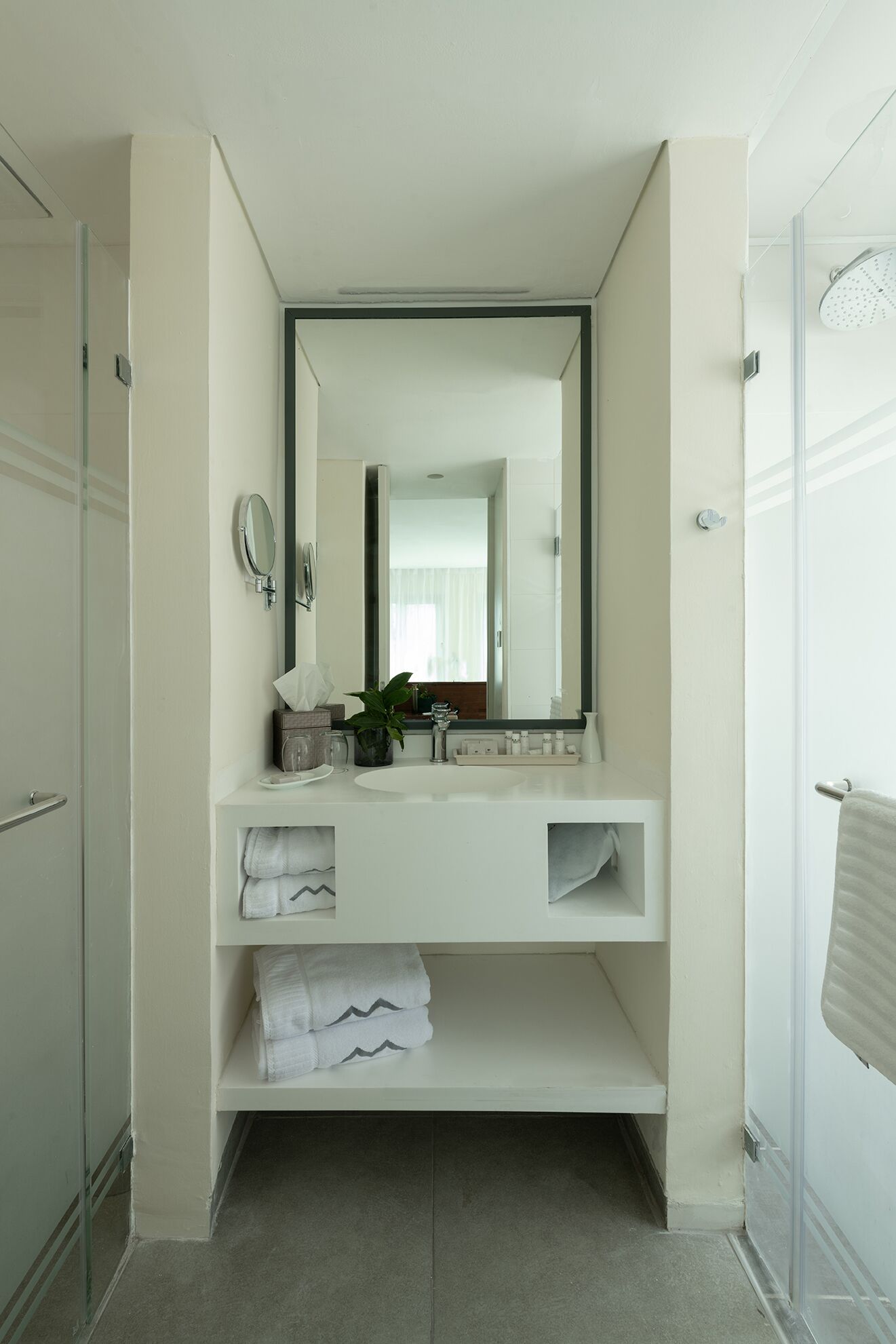 A modern bathroom with a white vanity, a large mirror, a towel rack, and a shower area.