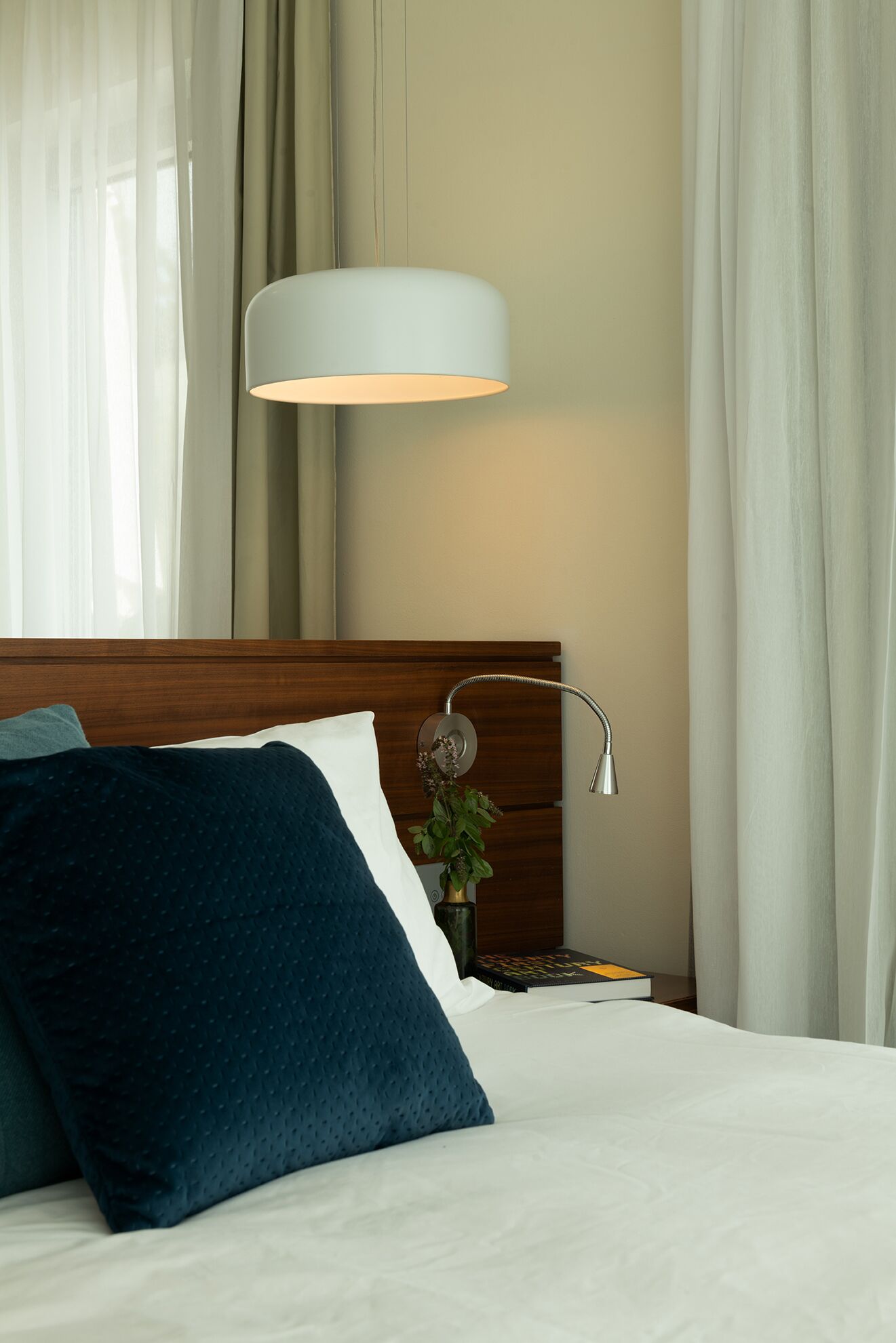 A neatly made bed with a white and blue pillow, a wooden headboard, a bedside table with a lamp, and a plant.