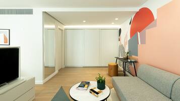 A modern living room with a flat-screen TV, a grey sofa, a coffee table with books and a plant, and a wall with abstract art.