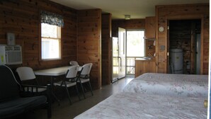 Une chambre de style cabane, comprenant un lit, un bureau avec des chaises, une fenêtre et une porte donnant sur l’extérieur.