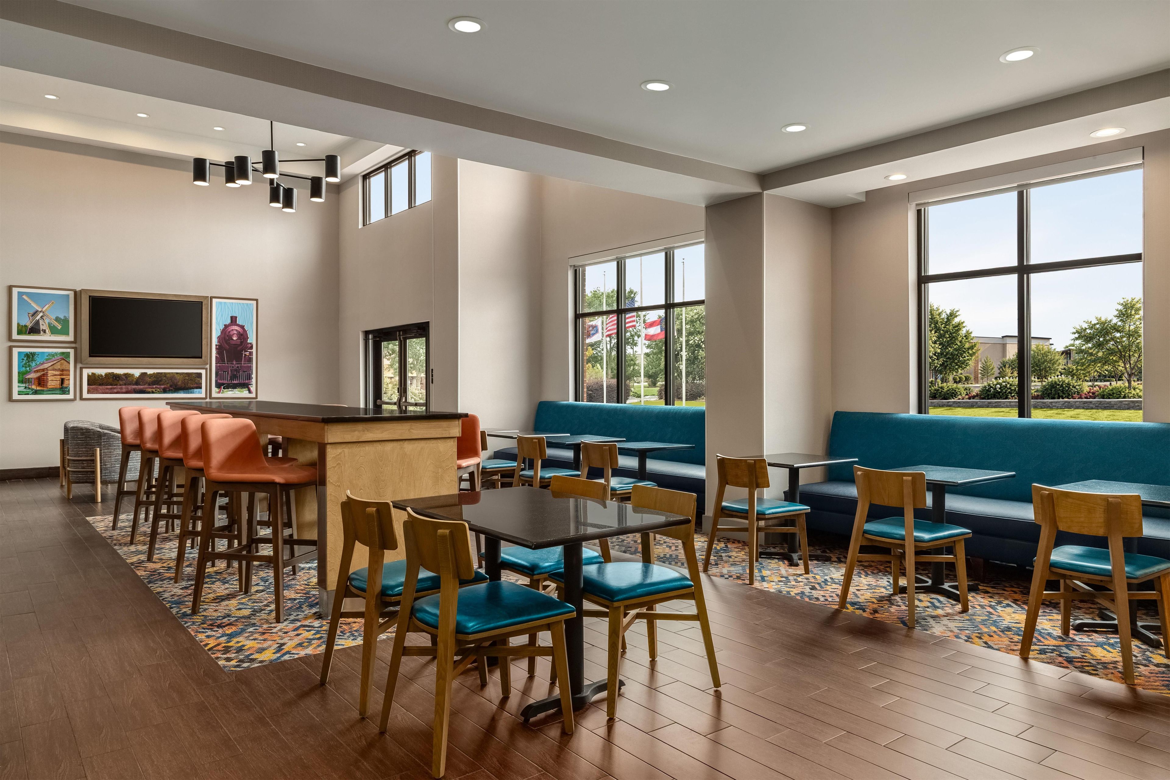 Un restaurante moderno con zona de bar, mesas y grandes ventanales con vistas al exterior.