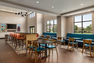 A modern restaurant with a bar area, seating arrangements, and large windows providing views of the outdoors.