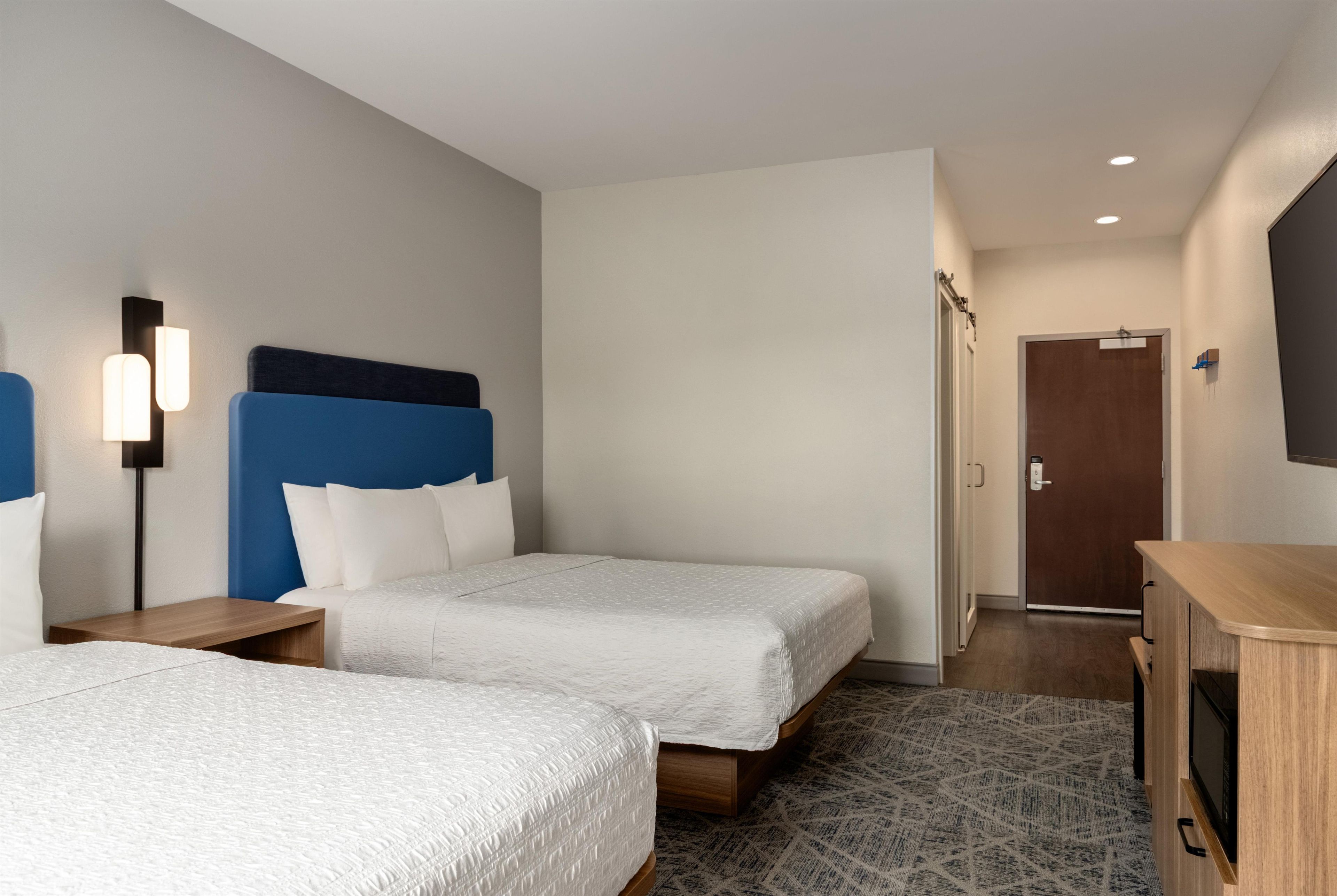 Habitación de hotel con dos camas, un escritorio, un armario y una puerta que da a otra habitación.