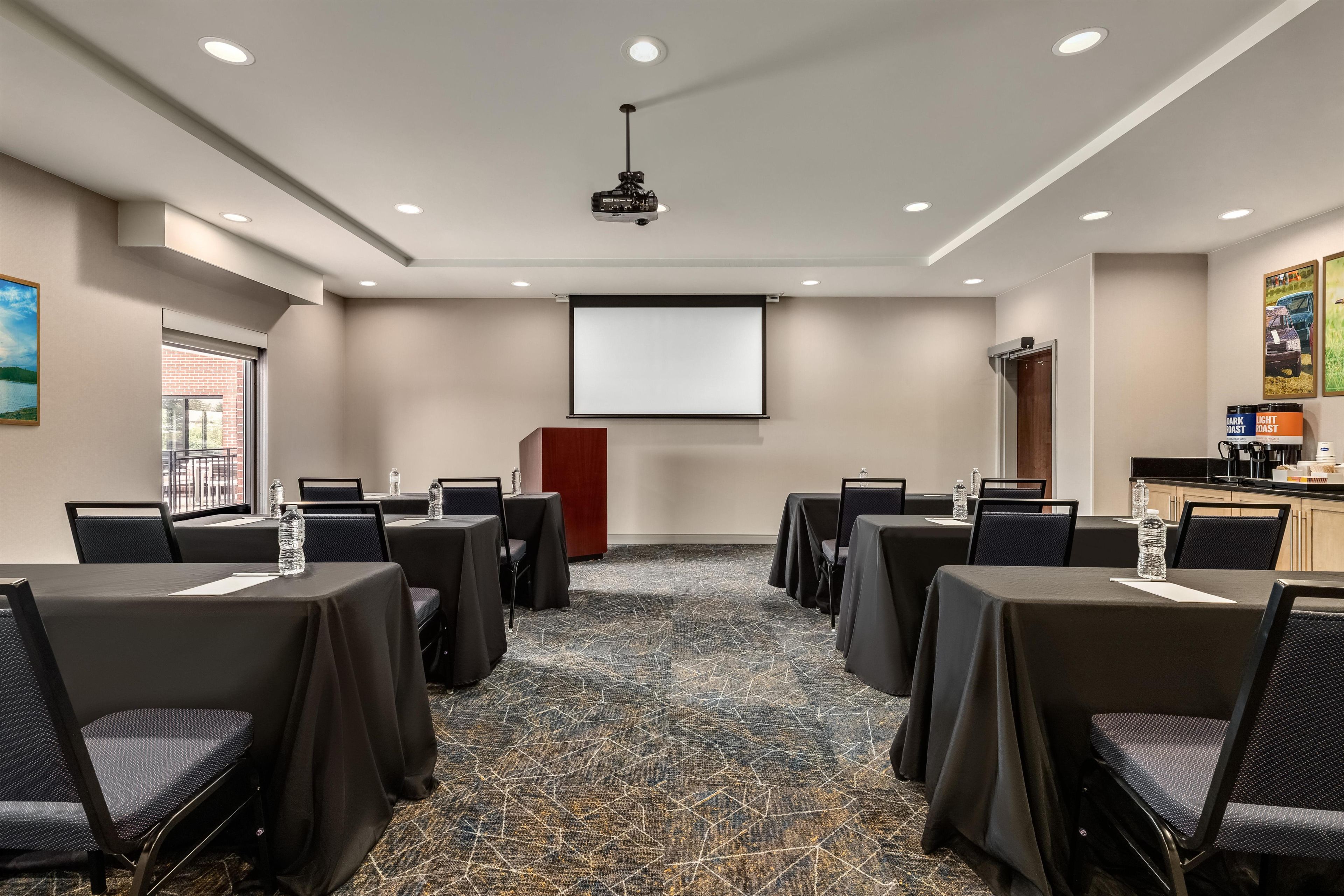 A conference room with tables, chairs, a projector, and a screen.