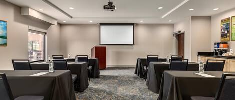 A conference room with tables, chairs, a projector, and a screen.