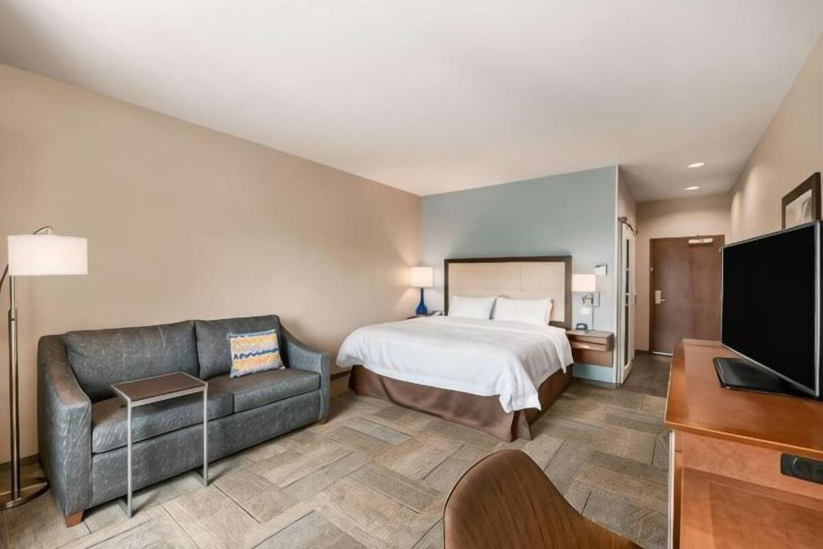 A hotel room with a bed, a sofa, a desk, a TV, and a lamp.