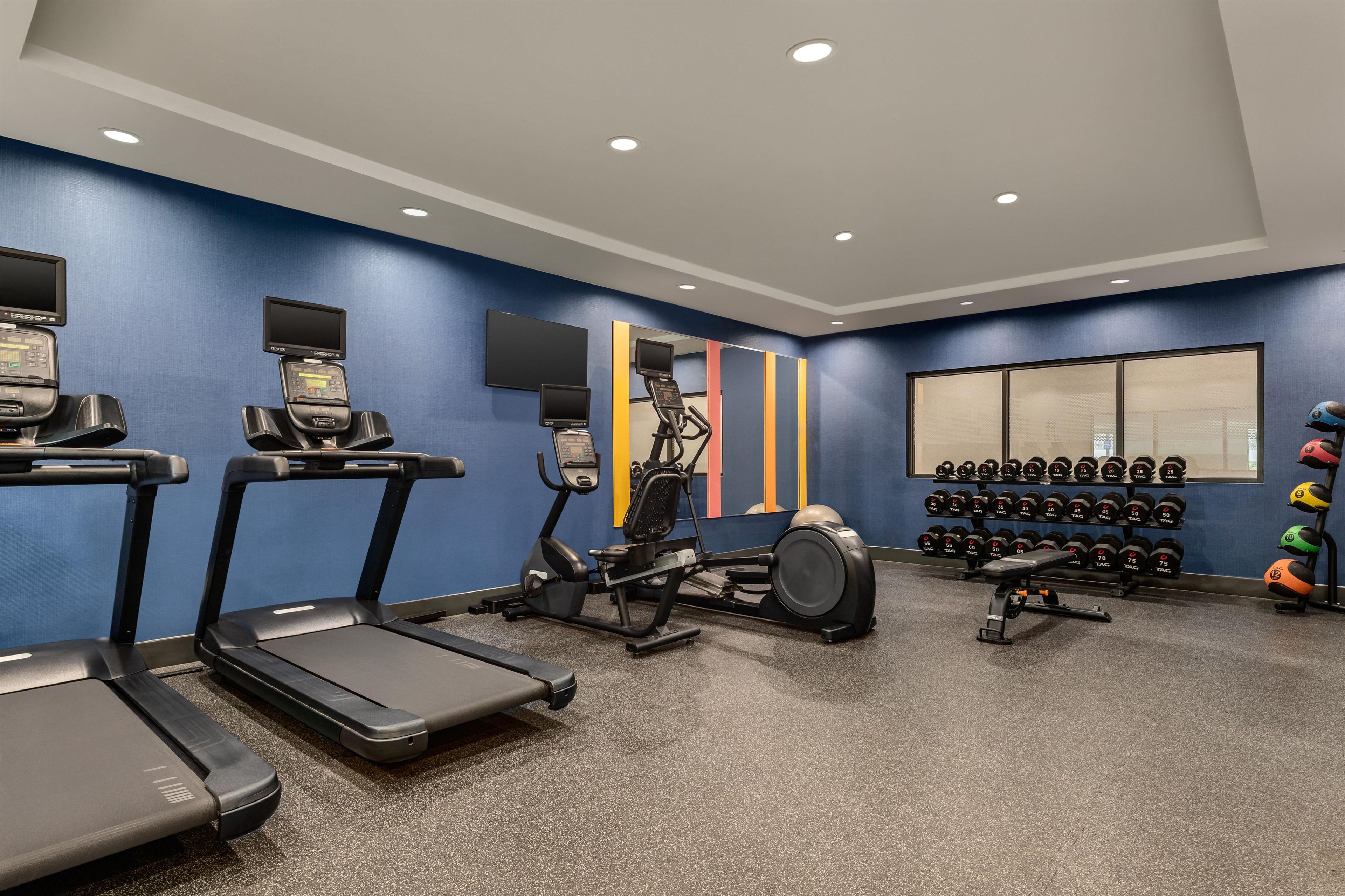 Un gimnasio con cintas de correr, elípticas, una máquina de remo y una pared llena de mancuernas.