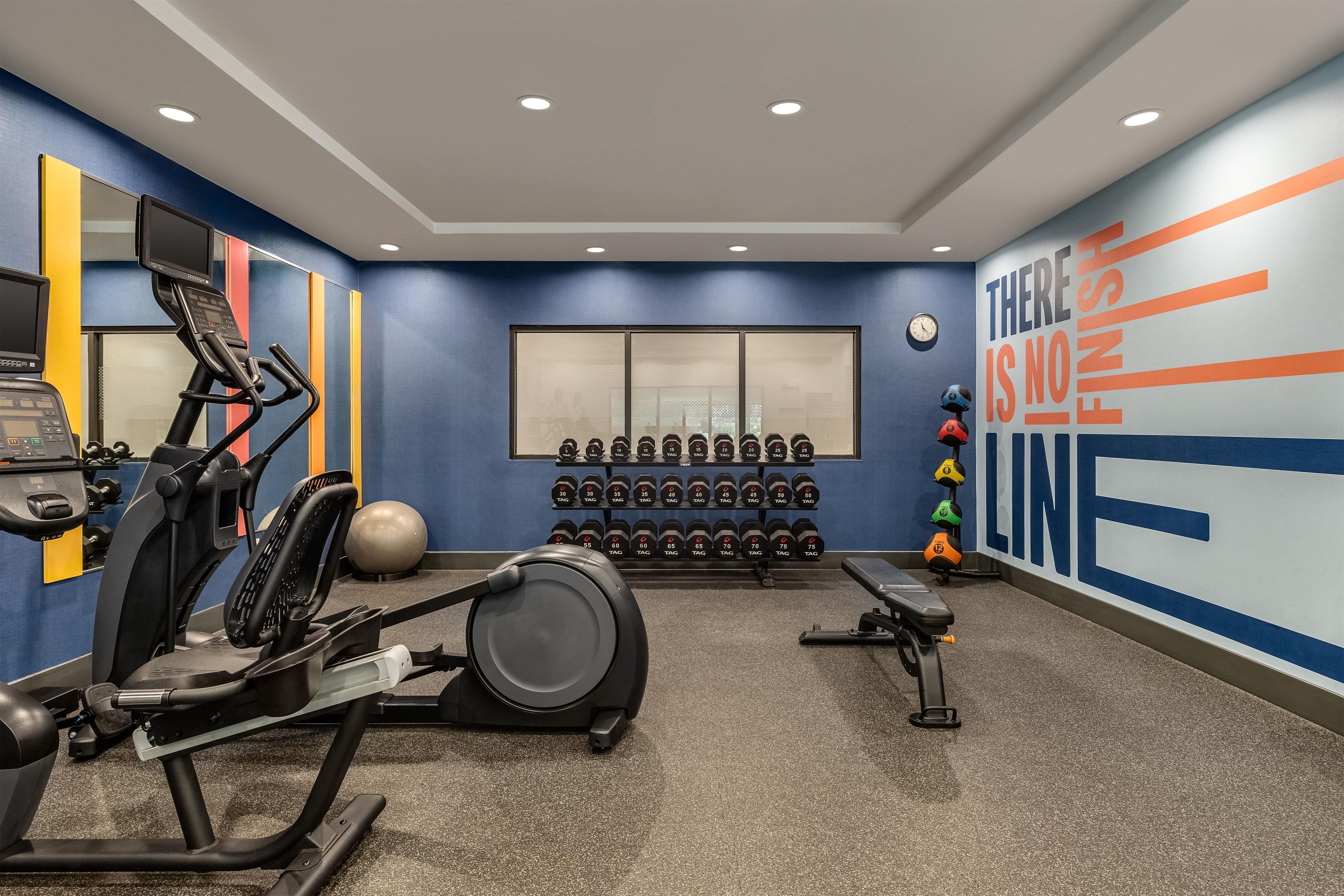 A gym with exercise equipment, dumbbells, and a motivational wall.