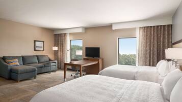 A hotel room with two beds, a desk, a television, and a sofa.