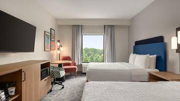 A hotel room with a bed, a desk, a chair, a flat-screen TV, and a window with a view of trees.