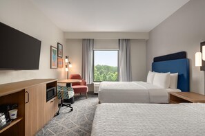 Habitación de hotel con cama, escritorio, silla, televisor de pantalla plana y ventana con vista a árboles.