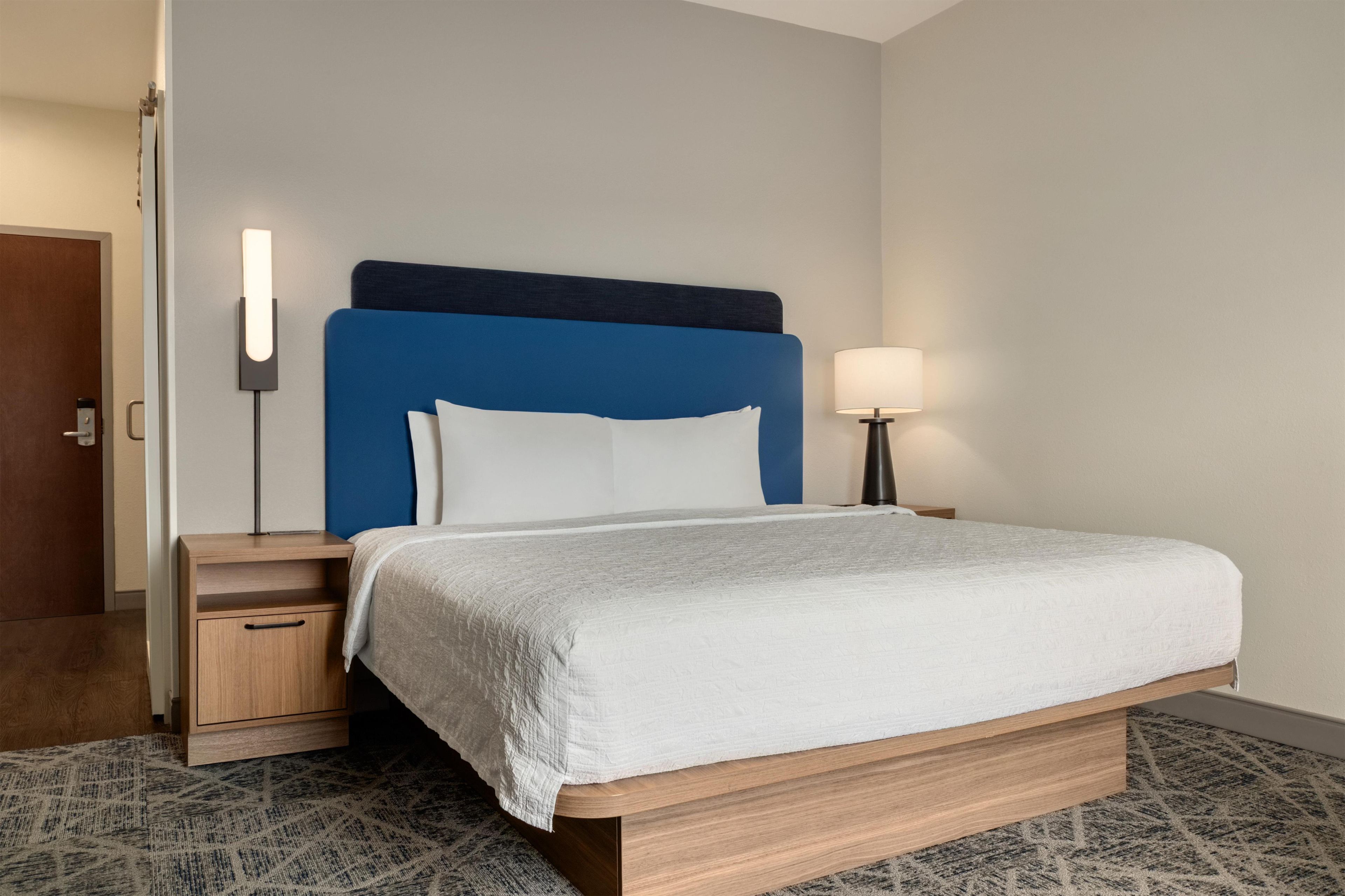 Una camera d'albergo con un letto, un comodino, una lampada e una porta.