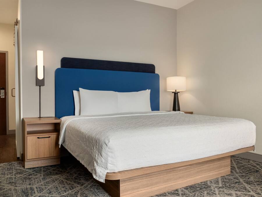 A hotel room with a bed, a nightstand, a lamp, and a door.
