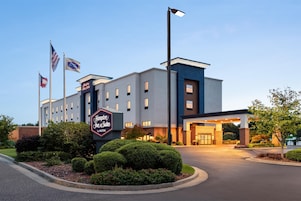 Hotel Hampton Inn & Suites by Hilton con un diseño moderno, que presenta una entrada destacada, exhibición de la bandera y jardinería bien cuidada.