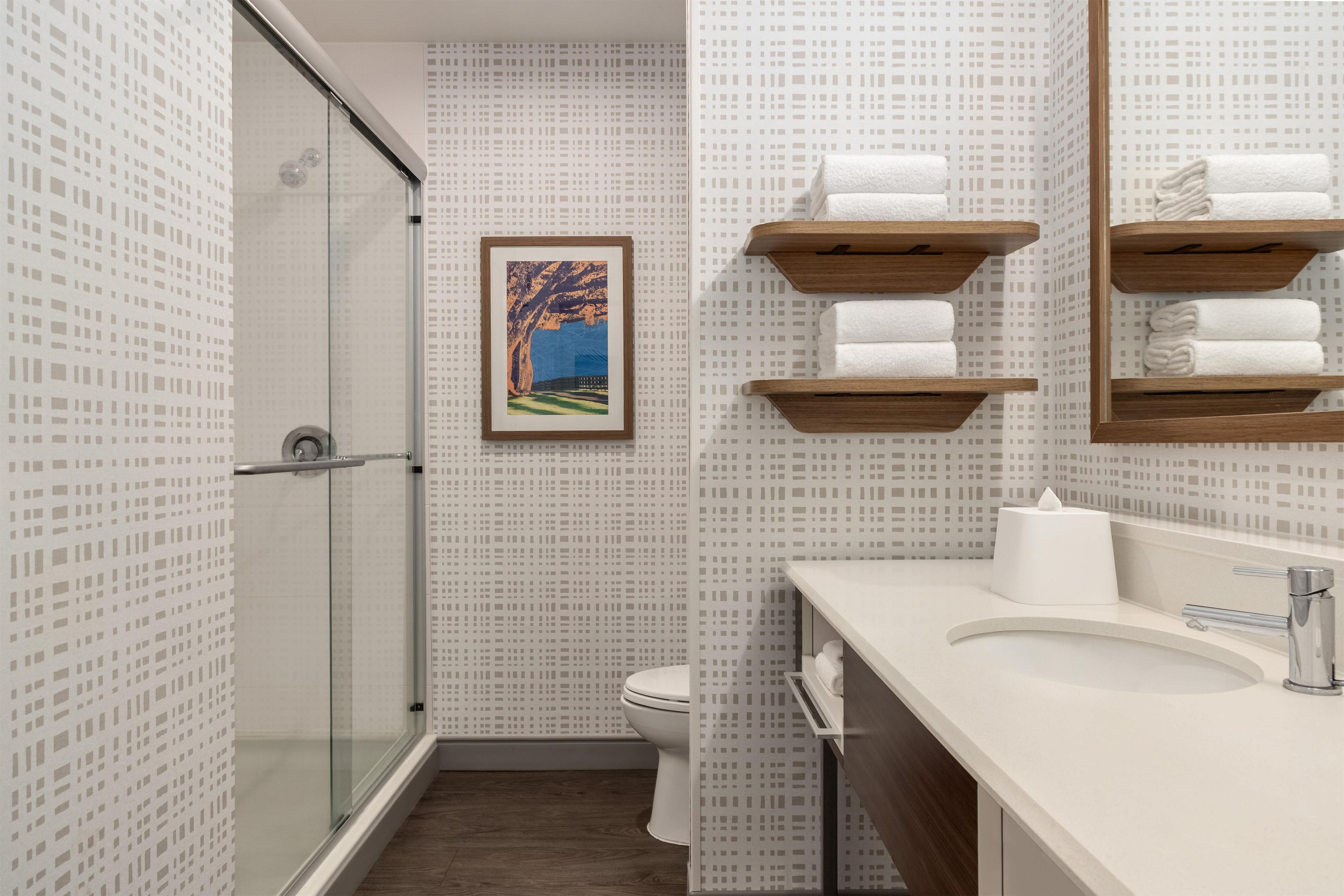 A modern bathroom with a glass shower enclosure, a toilet, a sink with a mirror, and wooden towel racks.