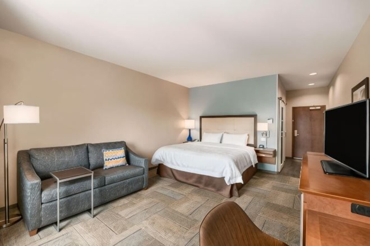 A hotel room with a bed, a sofa, a desk, a TV, and a lamp.