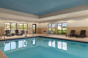 Un área de piscina con sillones de descanso y una mesa, ventanas amplias y vistas despejadas al exterior.
