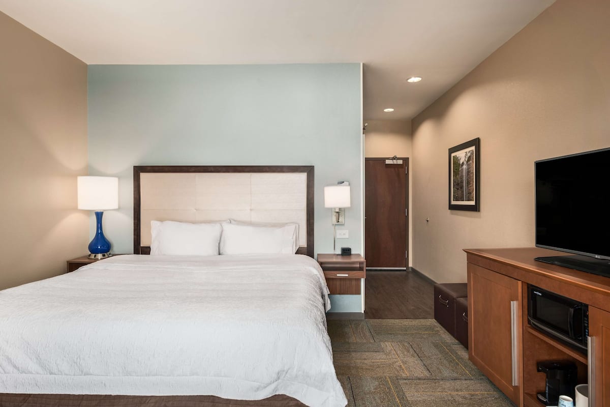 A hotel room with a large bed, bedside lamps, a TV, a coffee maker, and a wooden cabinet.
