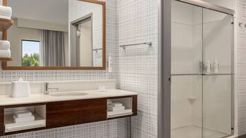 A modern bathroom with a large mirror, a sink, and a glass-enclosed shower.
