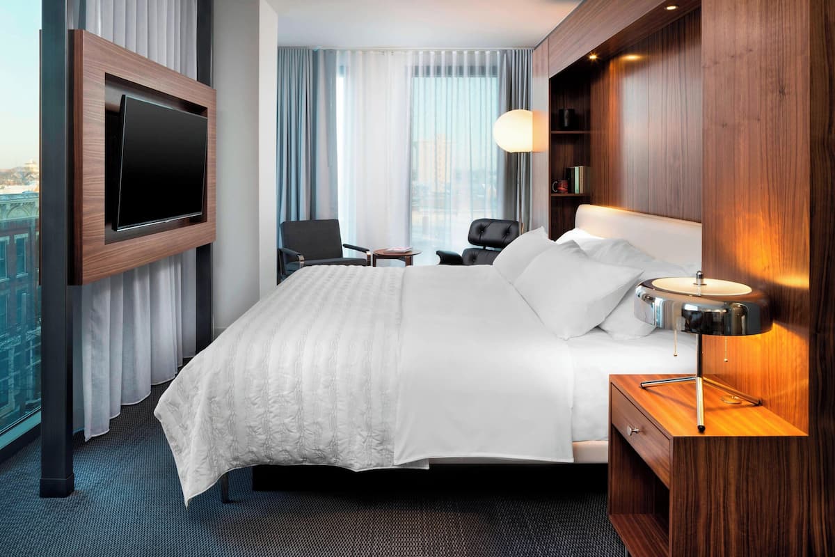 A hotel room with a large bed, a TV mounted on the wall, a desk, and a chair.
