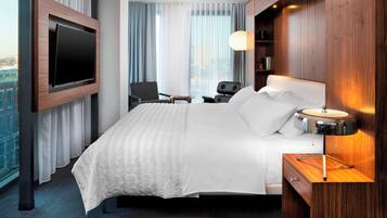 A hotel room with a large bed, a TV mounted on the wall, a desk, and a chair.