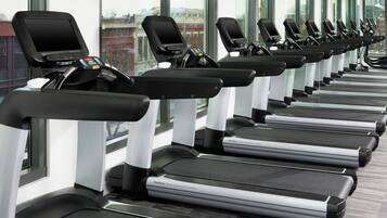 Une rangée de tapis de course dans une salle de sport dotée de grandes fenêtres et offrant une vue sur la ville.