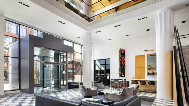 A spacious lobby with a checkered floor, modern furniture, and a glass wall leading to an outdoor area. - Le Méridien Columbus, The Joseph (Columbus)