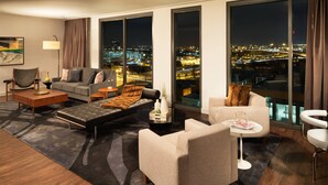 A modern hotel room with a city view, a sofa, a chair, a coffee table, and a small side table. - Le Méridien Columbus, The Joseph (Columbus)
