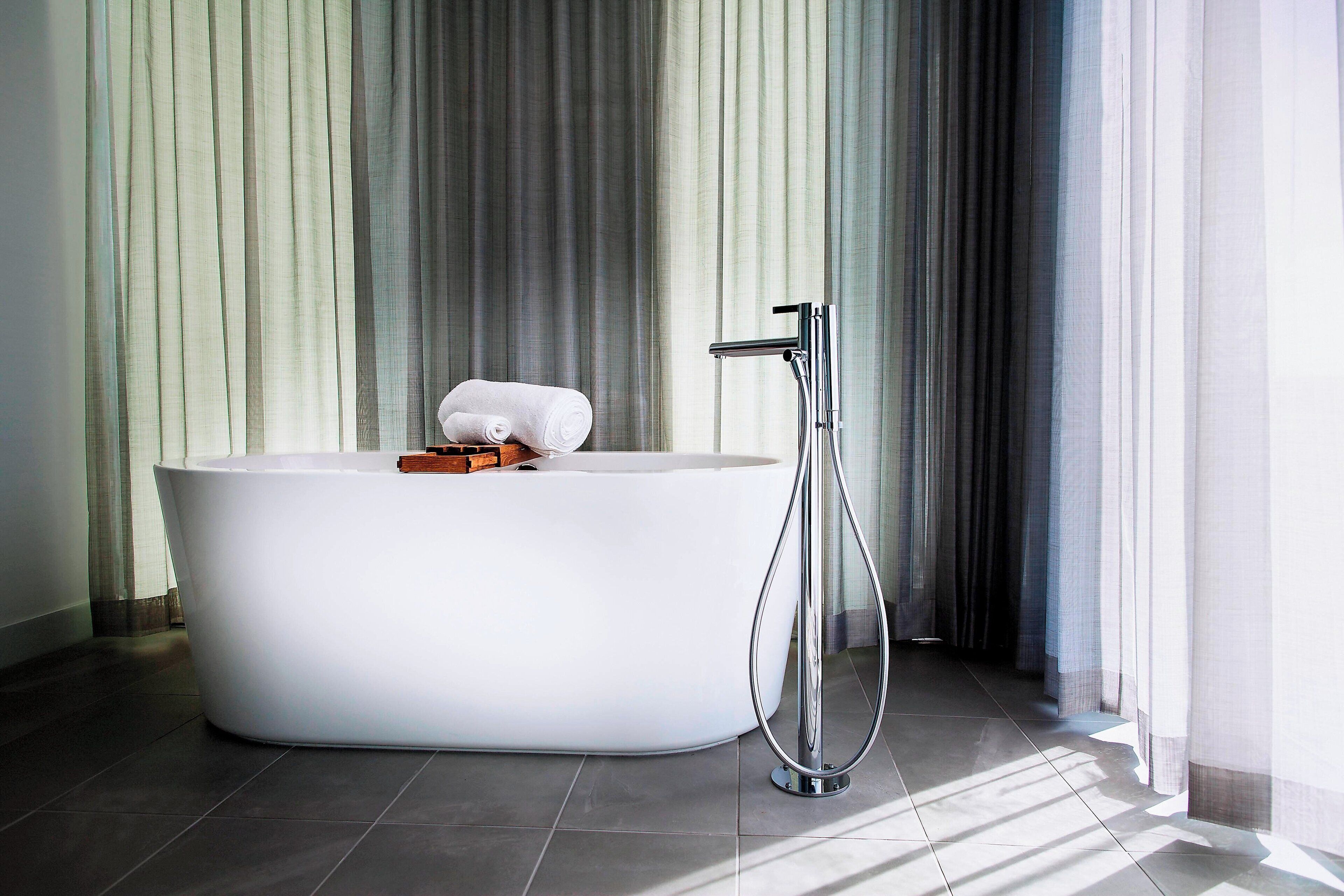 A modern bathroom with a freestanding bathtub, a handheld showerhead, and a towel on the edge.