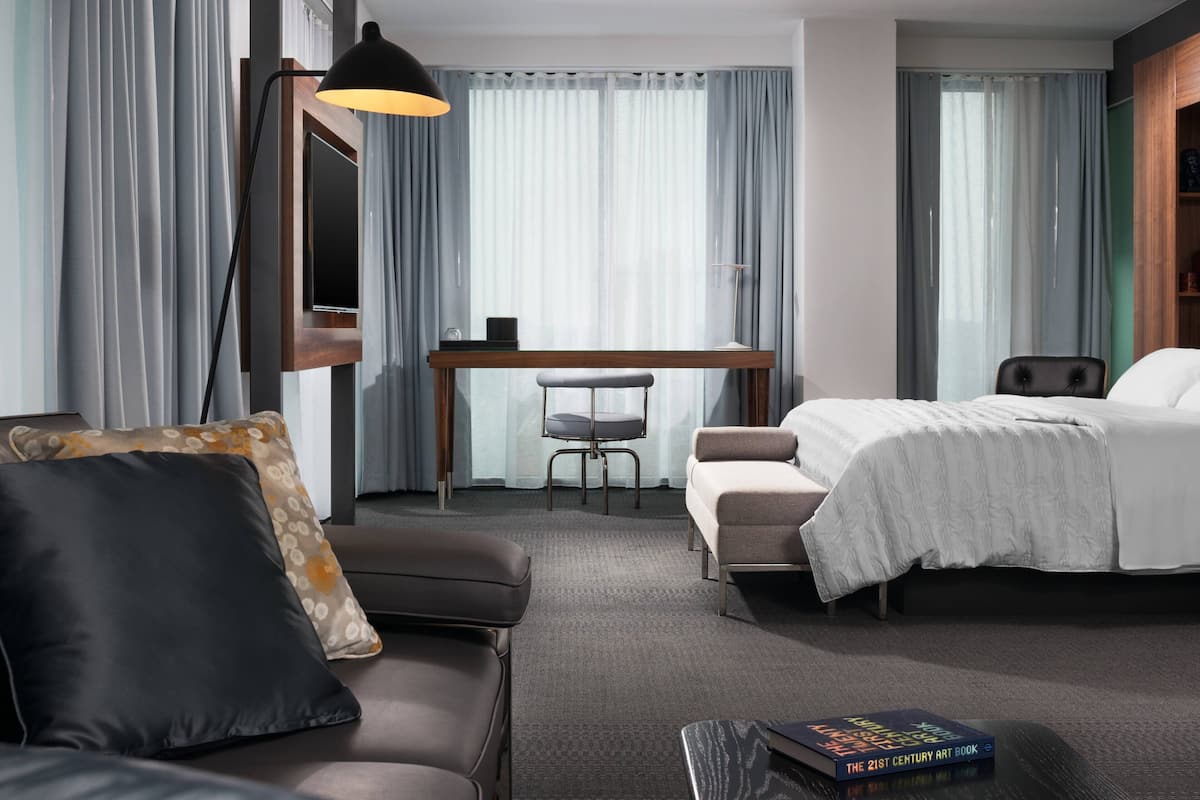 A hotel room with a bed, a desk, a chair, a sofa, and a lamp.