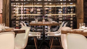 A dining area with a central table surrounded by chairs, a wine rack in the background, and a chandelier. - Le Méridien Columbus, The Joseph (Columbus)