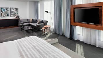 Hotelkamer met een groot bed, een bank, een eettafeltje, een aan de muur bevestigde televisie en een raam met gordijnen.