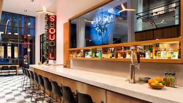 A bar area with a checkered floor, bar stools, a counter with a neon sign, and a large window with a digital art display.