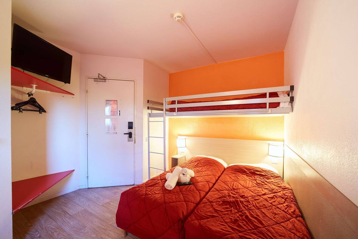 Een slaapkamer met een stapelbed, een rode spreidek en een aan de muur bevestigde televisie, plus een deur met een handgreep.