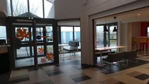A modern interior with a checkered floor, a seating area with tables and chairs, and a glass door with autumn leaf decals. - Premiere Classe Amiens (Amiens)
