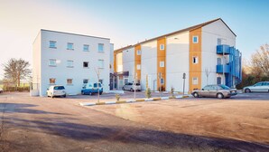 A modern building with a parking lot, featuring a mix of white and orange facades, and several cars parked in front. - Premiere Classe Amiens (Amiens)