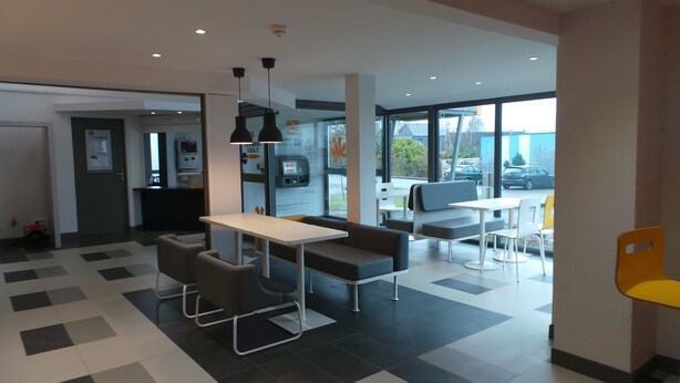 A modern indoor seating area with a table and chairs, a bench, and a view through large windows. - Premiere Classe Amiens (Amiens)