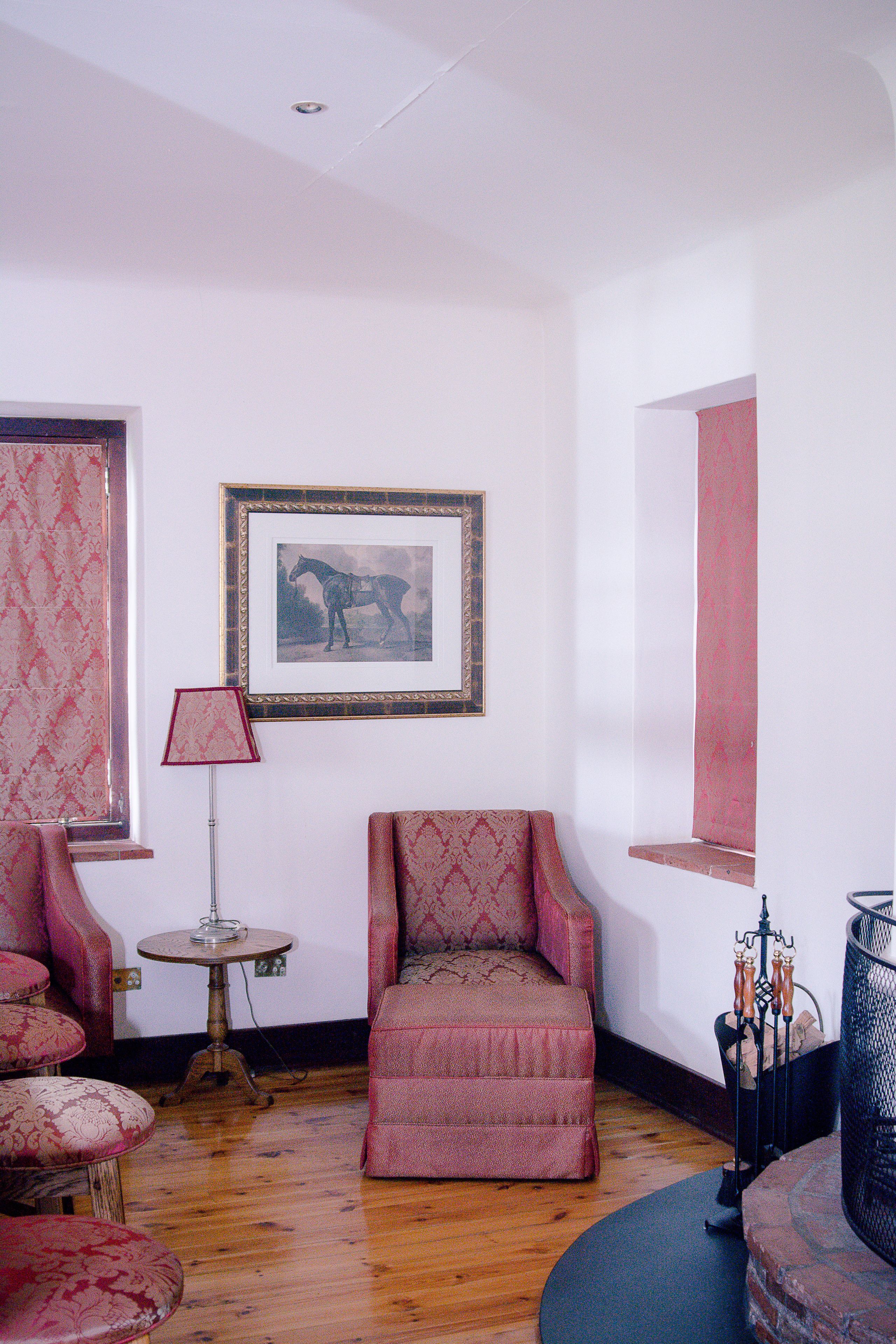 A room with a patterned armchair, a small round table, a framed picture on the wall, and a floor lamp.