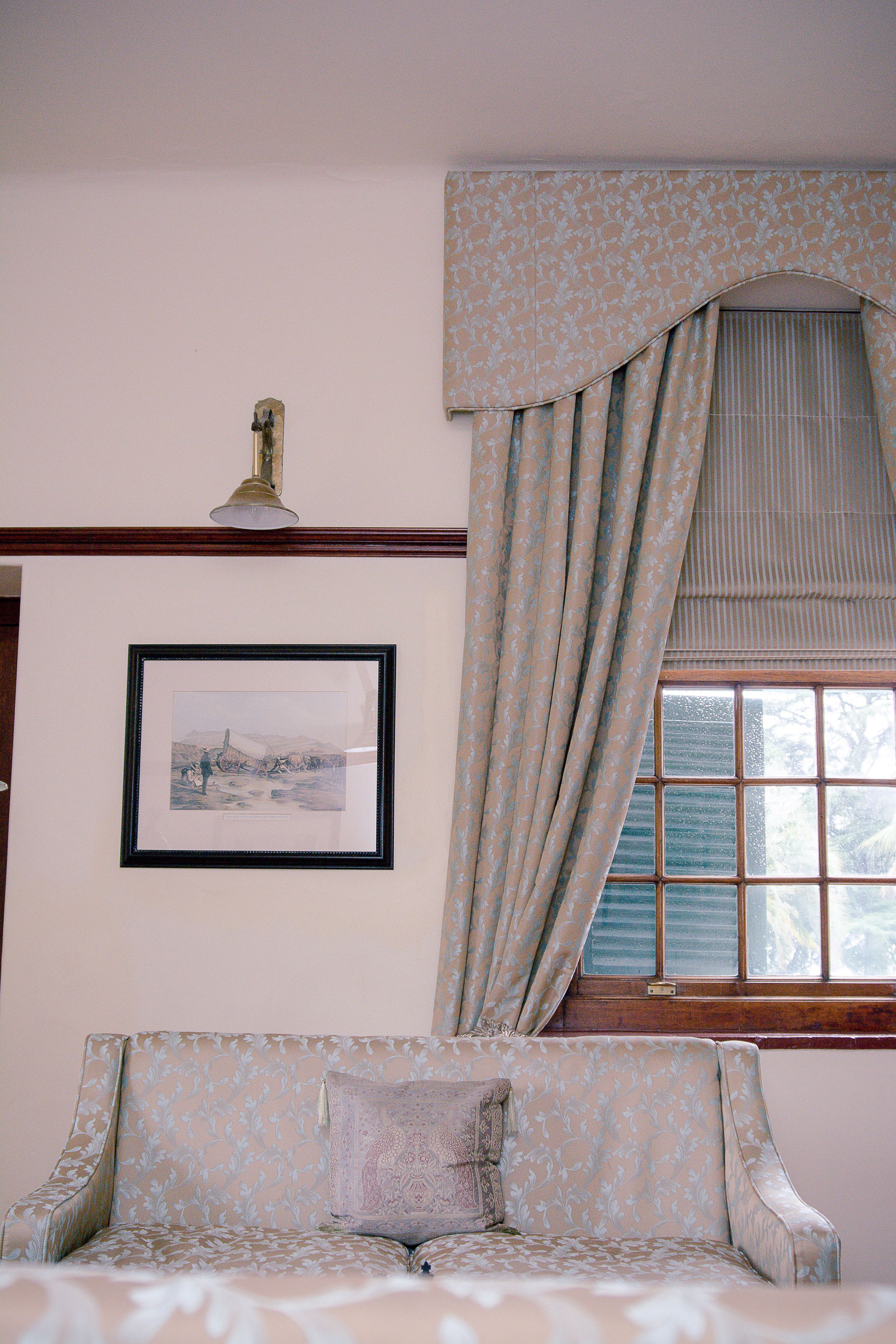 A room with a patterned sofa, a framed picture on the wall, and a window with curtains.