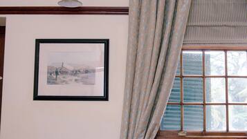 A room with a patterned sofa, a framed picture on the wall, and a window with curtains.