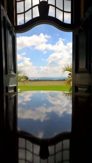 A view through a window with a decorative frame, reflecting a landscape with a clear sky, clouds, and greenery. - Welgelegen Manor (Dipaleseng)