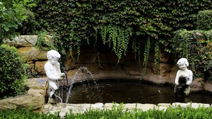 Un jardín con un estanque, dos estatuas de piedra y muros cubiertos de hiedra.