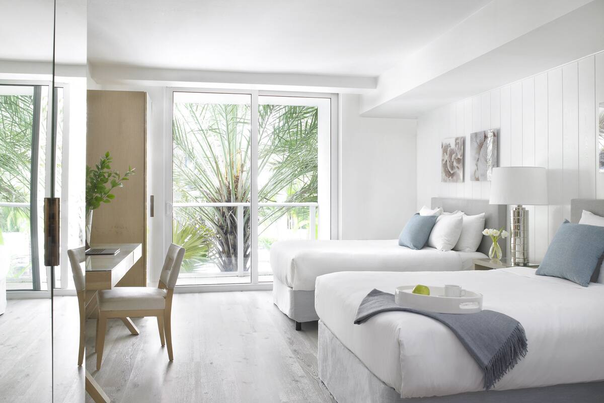 Une chambre d’hôtel moderne, dotée d’un grand lit, d’un bureau et offrant une vue sur les palmiers par les fenêtres.