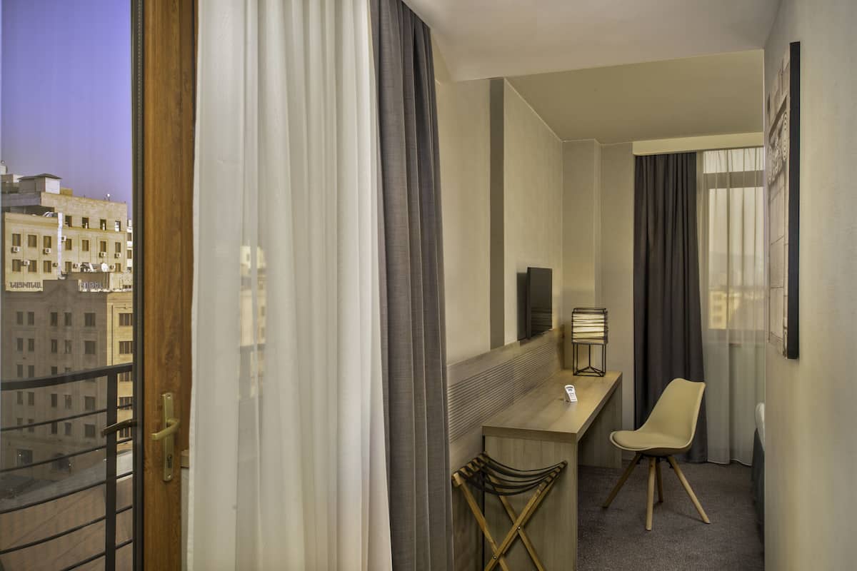 A hotel room with a balcony, a desk, a chair, and a bed.