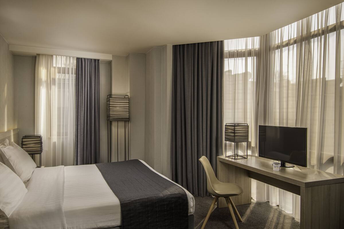 A hotel room with a bed, desk, chair, TV, and curtains.