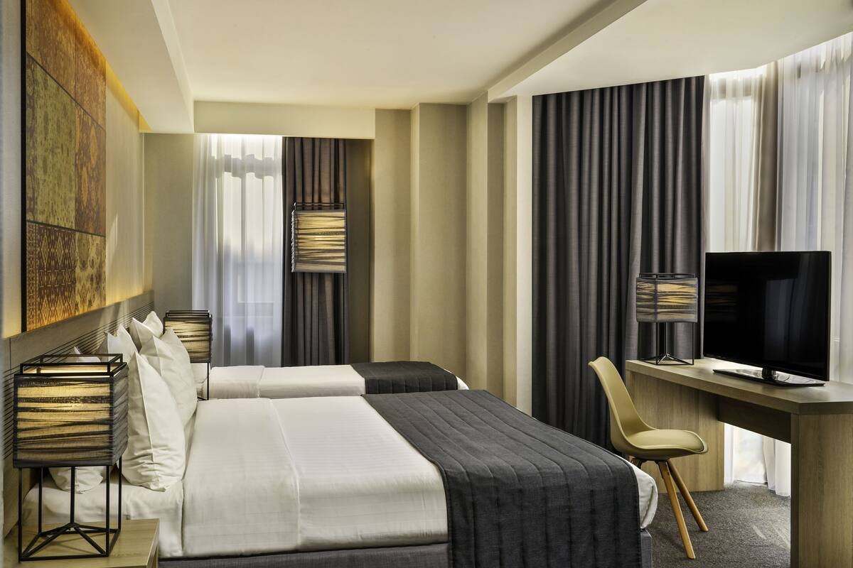 A hotel room with two beds, a desk, a television, and a chair.