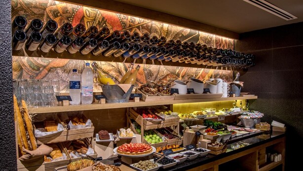 Un buffet proposant une variété d’aliments, notamment des fruits, des légumes et du pain. On y trouve également des bouteilles et des verres sur les étagères.